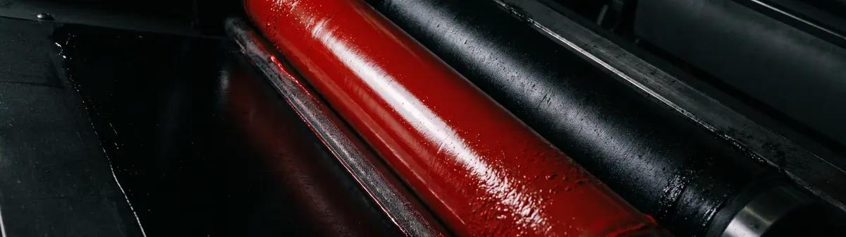 Un rodillo cargado de tinta roja junto a otro de tinta negra, dentro de una máquina de imprimir.